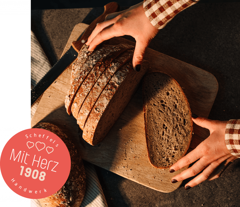 Ein Bild eines geschnittenen Brotes auf einem Brettchen. Auf der linken Seite befindet sich ein roter Kreis mit der Aufschrift Scheffels Handwerk – Mit Herz 1908