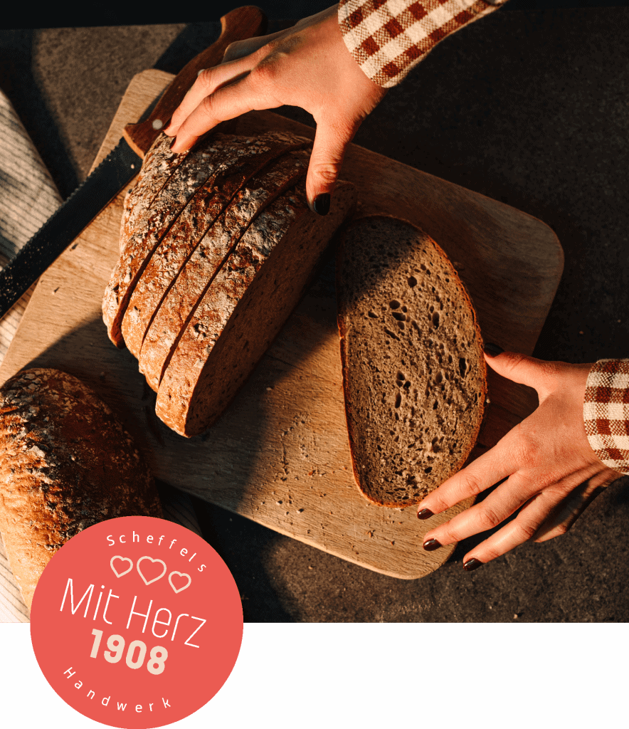 Ein Bild eines geschnittenen Brotes auf einem Brettchen. Auf der linken Seite befindet sich ein roter Kreis mit der Aufschrift Scheffels Handwerk – Mit Herz 1908